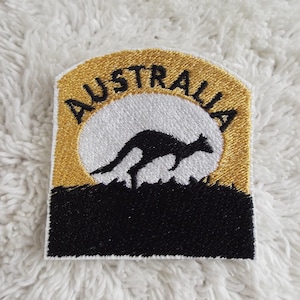 May include: A gold and black embroidered patch with the word "AUSTRALIA" in a semi-circle around a white silhouette of a kangaroo jumping in front of a white circle.