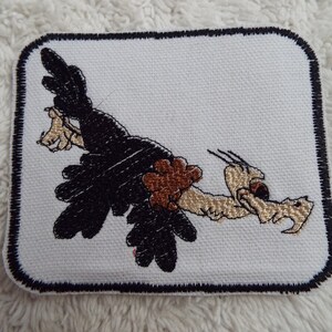 May include: A white embroidered patch with a black outline featuring a cartoon vulture with brown feathers and a yellow beak. The vulture is flying with its wings spread out.