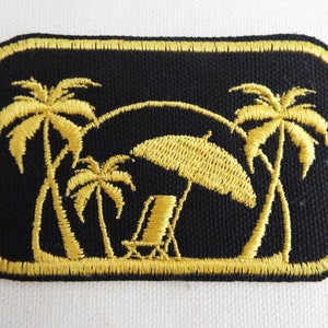 May include: A gold embroidered patch with a beach scene. The patch features three palm trees, a beach chair, and an umbrella.