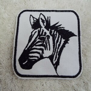 May include: Black and white embroidered iron-on patch of a zebra head. The patch is square shaped and has a black outline.