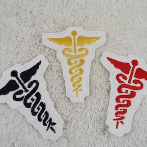 May include: Three embroidered iron-on patches featuring the medical symbol, a snake wrapped around a staff with wings. The patches are white with black, red, and gold embroidery.