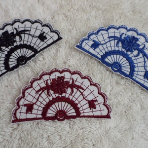 May include: Three embroidered fabric patches in the shape of a fan. The fan is white with a black, blue, and burgundy floral design.