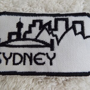 May include: Black and white embroidered patch with a skyline of Sydney, Australia and the word "SYDNEY" below.