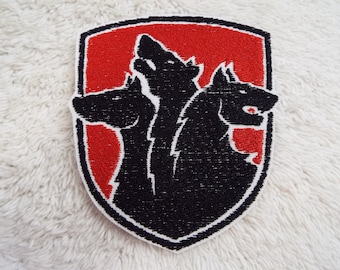 May include: A red and black embroidered patch featuring a three-headed wolf design. The wolf's heads are facing different directions, and the patch is shaped like a shield.