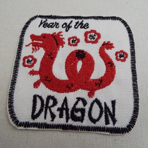 May include: A white embroidered patch featuring a red dragon and the text "Year of the Dragon".