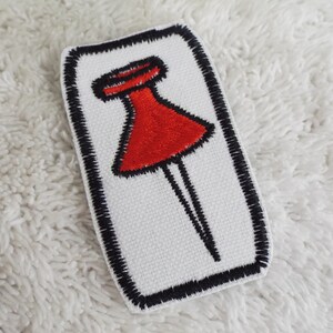 May include: An iron-on patch embroidered with a red and black push pin.