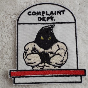 May include: White embroidered patch with a black hooded figure with yellow eyes, arms crossed, and the text "COMPLAINT DEPT." above the figure.