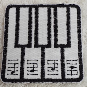 May include: Square, white patch with a black embroidered piano keyboard design. The keyboard has black keys and is bordered by a black stitched edge. Below the keyboard are black musical notes.