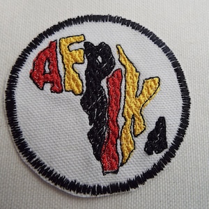 May include: An embroidered patch featuring an outline of the continent of Africa in black, red and gold. The word "AFRIK" is spelled out within the outline of the continent.