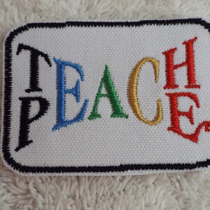 May include: A white embroidered patch with a black border. The word "TEACH" is embroidered in colorful letters. The "T" is black, the "E" is blue, the "A" is green, the "C" is gold, and the "H" is red.