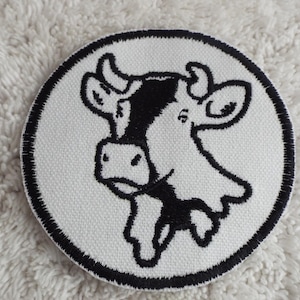 Peut inclure: Un patch brodé noir et blanc représentant une tête de vache dans un cercle. Le patch est sur un fond blanc.