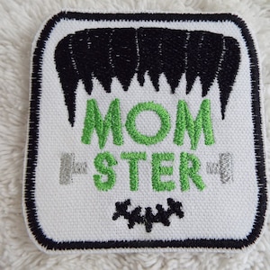 May include: White embroidered patch with black stitching. The patch features a black and white graphic of a monster's hair, the text "MOM-STER" in green, and a row of black stitches at the bottom.