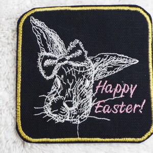 May include: White embroidered bunny rabbit with a pink bow on a black background with the text "Happy Easter!" in pink.