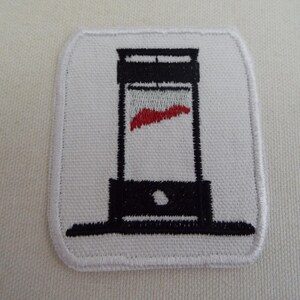 May include: White embroidered patch featuring a black guillotine design with a red blade. The patch has a white border and is square with rounded corners. The design is centered on the patch.