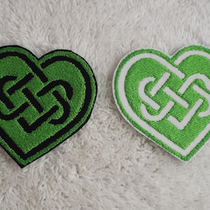 May include: Two green heart-shaped patches with a Celtic knot design. One patch has a black outline and the other has a white outline.