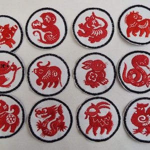 Puede incluir: Doce parches bordados que representan los animales del zodíaco chino. Cada parche es circular, con fondo blanco y borde negro. Los animales son rojos y están dispuestos en una cuadrícula.