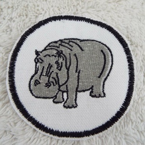 May include: A white round iron-on patch with a black border featuring a gray embroidered hippopotamus.