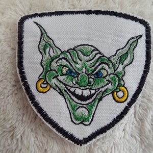May include: Green embroidered patch of a goblin with large ears, a mischievous grin, and gold hoop earrings. The patch is on a white background with a black border.