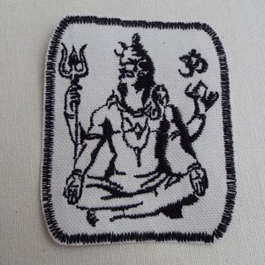 Puede incluir: Parche bordado en blanco y negro con una deidad sosteniendo un tridente, sentada en una postura meditativa con un símbolo sobre la cabeza.