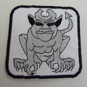 Könnte beinhalten: Ein grauer gestickter Bügeleisen-Aufnäher mit einem Cartoon-Gargoyle mit einem zahnigen Grinsen und einem eingerollten Schwanz.