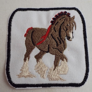 May include: Embroidered patch featuring a brown horse with a red mane and tail, white feet, and a red bridle. The horse is walking to the right. The patch is bordered in black.