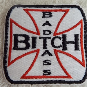 May include: White embroidered patch with a red cross and the words "BITCH" and "BADASS" written vertically.