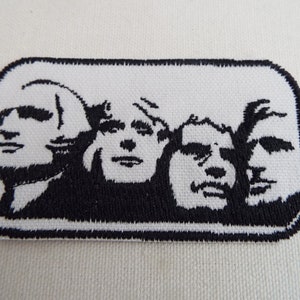May include: Embroidered patch showing Mount Rushmore in black and white. The patch is rectangular with rounded corners and a black border. The faces of the four presidents are clearly depicted.