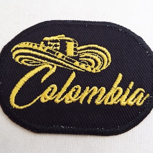 May include: A black embroidered patch with a yellow sombrero and the word "Colombia" in a stylized font.
