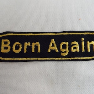 May include: Black and gold embroidered patch with the text "Born Again" in a rectangular shape.