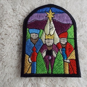 May include: An embroidered patch depicting the three wise men in a stained glass window style. The men are wearing colorful robes and holding gifts. A star shines above them.