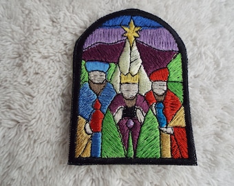 May include: An embroidered patch depicting the three wise men in a stained glass window style. The men are wearing colourful robes and holding gifts. A star shines above them.