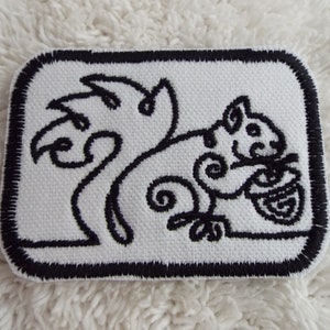 May include: Black and white embroidered patch of a squirrel holding a nut. The patch is rectangular with a black border and is on a white background.