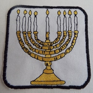 May include: A gold embroidered menorah with seven candles, set against a white background with a black border.