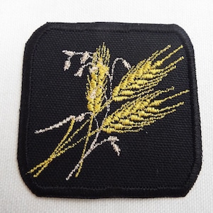 May include: A black square patch with embroidered wheat stalks in gold and white.