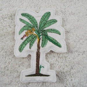 May include: Embroidered patch of a green palm tree with a brown trunk and yellow flowers. The patch is on a white background.