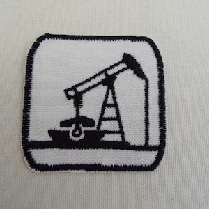May include: A square patch with a black and white design of an oil pump jack. The image is embroidered on a white background with a black stitched border. The oil pump jack is black.