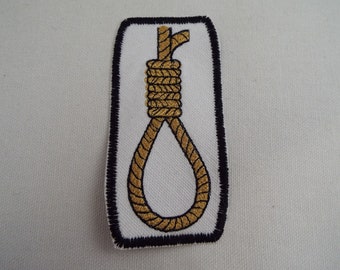 Könnte beinhalten: Ein gestickter schwarzer und weißer Aufnäher mit einer goldenen Strickschlinge.