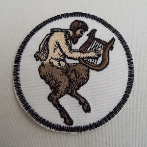 May include: A white embroidered patch with a black border, featuring a brown and tan centaur playing a lyre.