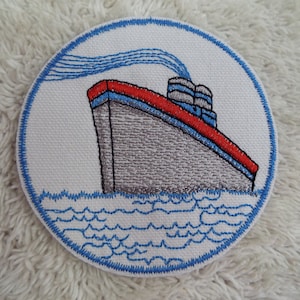 May include: A round, white embroidered patch with a blue border. The patch features a gray and red ship with blue smoke coming from the smokestack. The ship is sailing on blue waves.