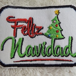 May include: A white embroidered patch with a green Christmas tree and the text "Feliz Navidad" in red and green lettering.