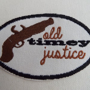 May include: A white oval embroidered patch with a brown pistol and the text "old timey justice" in brown thread.