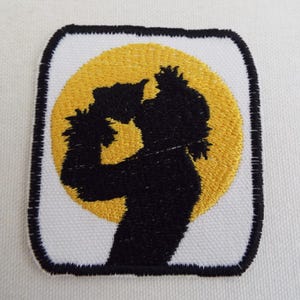 May include: Embroidered patch with a black silhouette of a person drinking from a cup, set against a yellow circle on a white background.