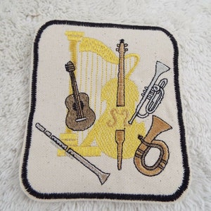 May include: Embroidered patch featuring a variety of musical instruments, including a harp, guitar, cello, trumpet, and a French horn. The patch is beige with a black border.