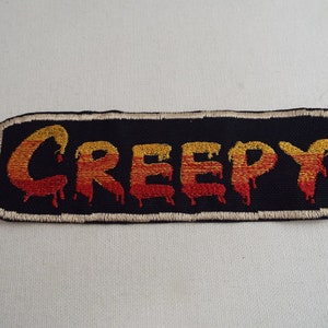 May include: A black embroidered patch with the word "CREEPY" in dripping red and yellow letters.