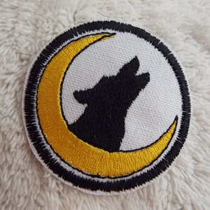 May include: A black embroidered wolf howling at a yellow crescent moon on a white background. The design is surrounded by a black outline.