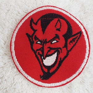 May include: Red embroidered patch with a white outline, featuring a black and white cartoon devil with horns and a mischievous grin.