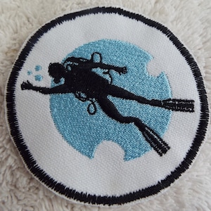 Könnte beinhalten: Ein weißer gestickter Aufnäher mit schwarzem Rand, der einen Taucher in Silhouette vor einem blauen Kreis zeigt.