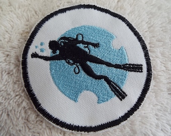 Könnte beinhalten: Ein weißer gestickter Aufnäher mit schwarzem Rand, der einen Taucher in Silhouette vor einem blauen Kreis zeigt.