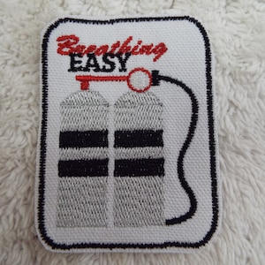 Puede incluir: Parche blanco bordado con una llave roja y el texto "Breathing Easy" sobre dos tanques de buceo grises con bandas negras.