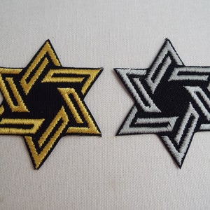 Op de afbeelding: Twee geborduurde strijkpatches in de vorm van een zespuntige ster. Eén patch is goud en de andere is zilver.